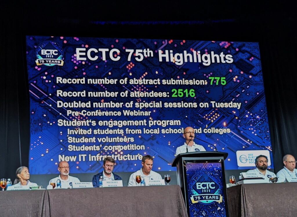 Presenters seated at a long table with one speaker and a slide highlighting successes behind them.